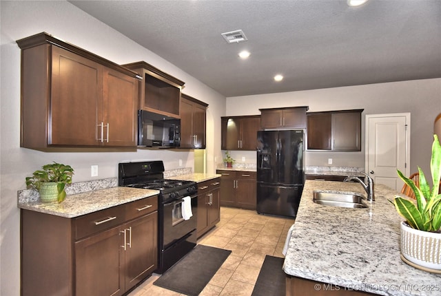 kitchen featuring dark brown cabinetry, sink, light tile patterned floors, light stone countertops, and black appliances