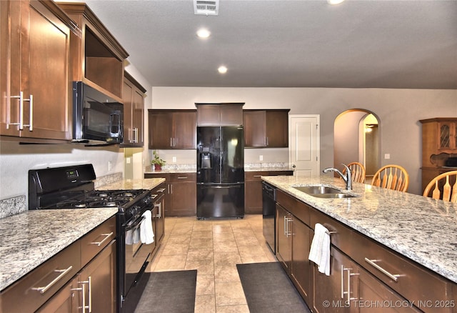 kitchen with a breakfast bar, sink, light tile patterned floors, black appliances, and light stone countertops