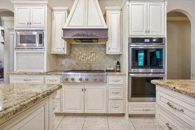 6215 E 86th Pl, Tulsa, OK 74137 - kitchen featuring custom exhaust hood, light tile patterned floors, appliances with stainless steel finishes, light stone countertops, and decorative backsplash