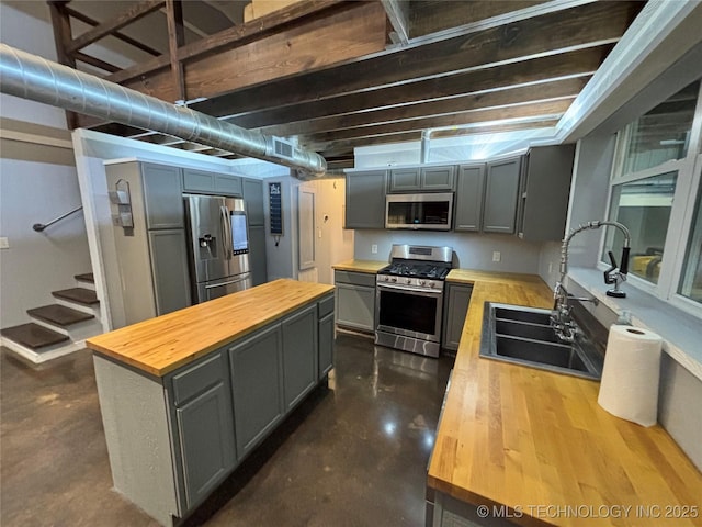 kitchen featuring sink, appliances with stainless steel finishes, gray cabinetry, wood counters, and concrete floors