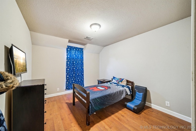 bedroom featuring light hardwood / wood-style flooring, a textured ceiling, and vaulted ceiling