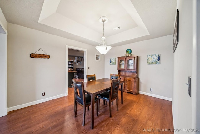 dining area with dark hardwood / wood-style flooring and a raised ceiling