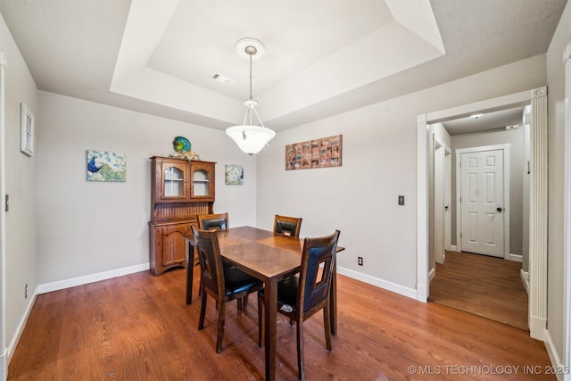 dining room with dark wood-type flooring and a tray ceiling