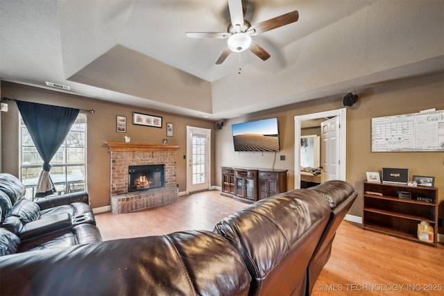 living room featuring ceiling fan, a raised ceiling, a brick fireplace, and light wood-type flooring