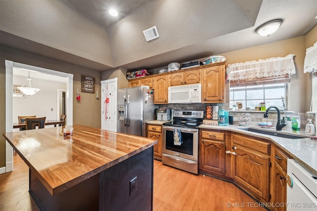 kitchen with wood counters, tasteful backsplash, sink, stainless steel appliances, and light wood-type flooring