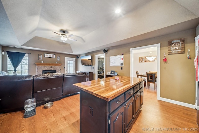 kitchen featuring dark brown cabinetry, light wood-type flooring, wood counters, and a tray ceiling