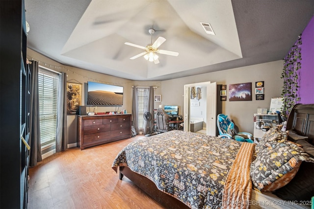 bedroom featuring ceiling fan, a raised ceiling, a textured ceiling, and light wood-type flooring