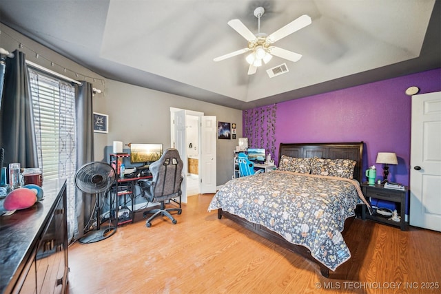 bedroom with a raised ceiling, wood-type flooring, and ceiling fan