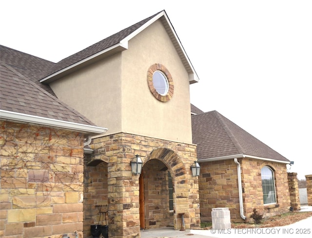 exterior space featuring stucco siding, stone siding, and roof with shingles