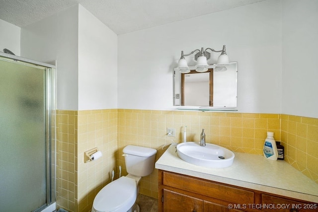 bathroom with tile walls, vanity, a textured ceiling, a shower with shower door, and toilet