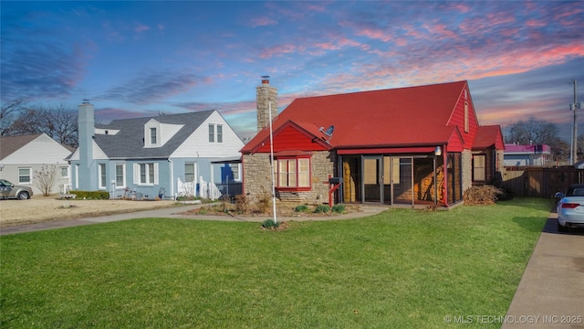 view of front facade with stone siding, a chimney, a front yard, and fence