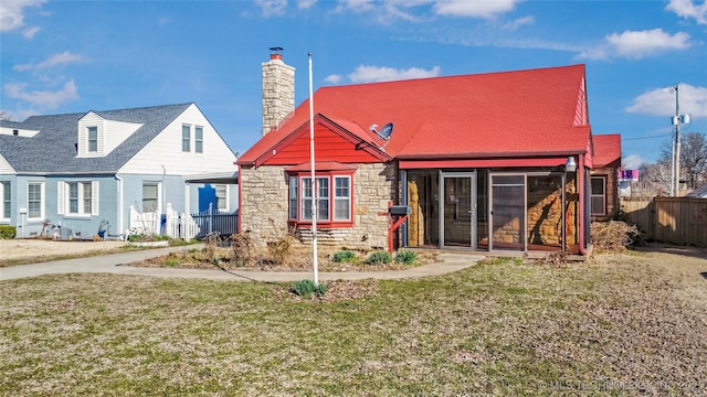 back of house with fence, a lawn, a chimney, a sunroom, and stone siding