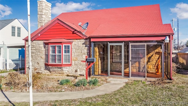 bungalow featuring fence, stone siding, a sunroom, and a chimney