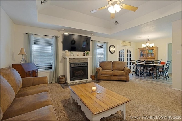 living room with a healthy amount of sunlight, a raised ceiling, and ceiling fan with notable chandelier