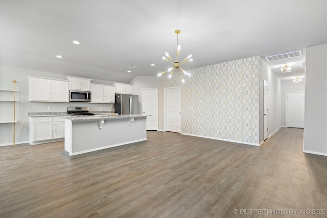 kitchen with a breakfast bar area, white cabinets, a kitchen island with sink, light stone counters, and stainless steel appliances