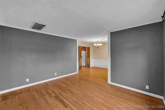 spare room with hardwood / wood-style flooring, ornamental molding, a textured ceiling, and a notable chandelier