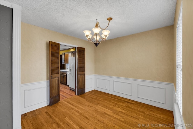 unfurnished room featuring a textured ceiling, a chandelier, and light wood-type flooring