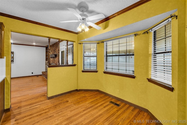 unfurnished room with crown molding, a healthy amount of sunlight, a textured ceiling, and light wood-type flooring