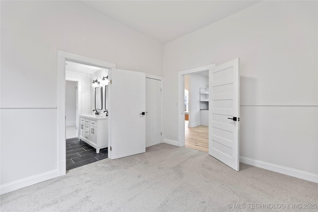 unfurnished bedroom with ensuite bathroom, sink, and dark carpet