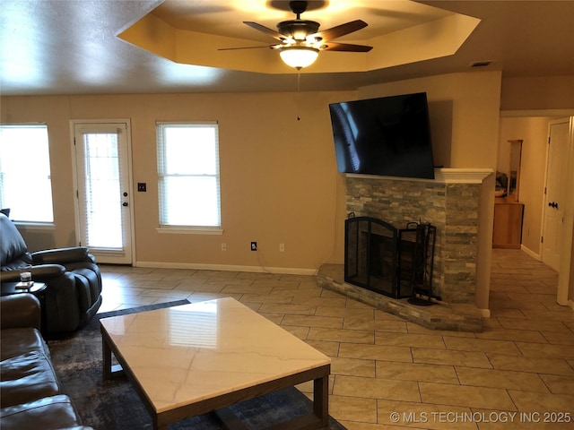 living room with a tray ceiling, a fireplace, and ceiling fan