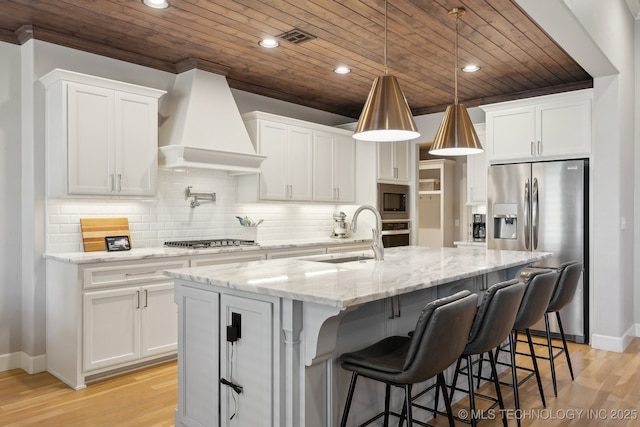 kitchen with appliances with stainless steel finishes, white cabinets, premium range hood, and a sink