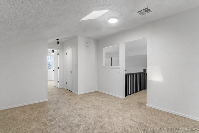 unfurnished room with light colored carpet, a skylight, and a textured ceiling