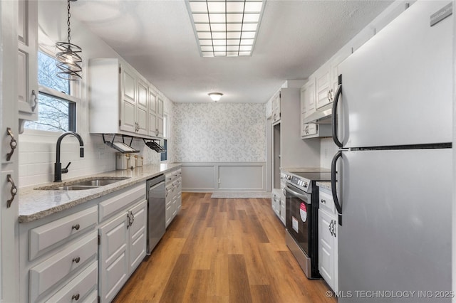 kitchen featuring sink, white cabinetry, hanging light fixtures, hardwood / wood-style flooring, and stainless steel appliances