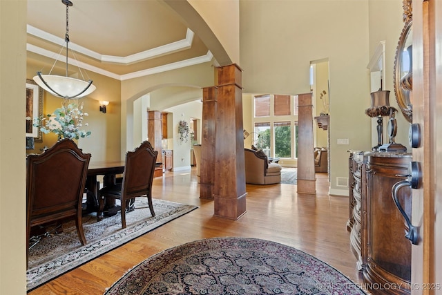 foyer with crown molding, light hardwood / wood-style flooring, a towering ceiling, decorative columns, and a raised ceiling