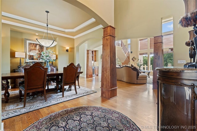 dining room featuring ornate columns, crown molding, light wood-type flooring, a tray ceiling, and a high ceiling