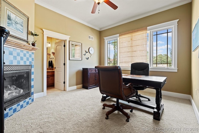 office area with a tiled fireplace, ornamental molding, light carpet, and ceiling fan