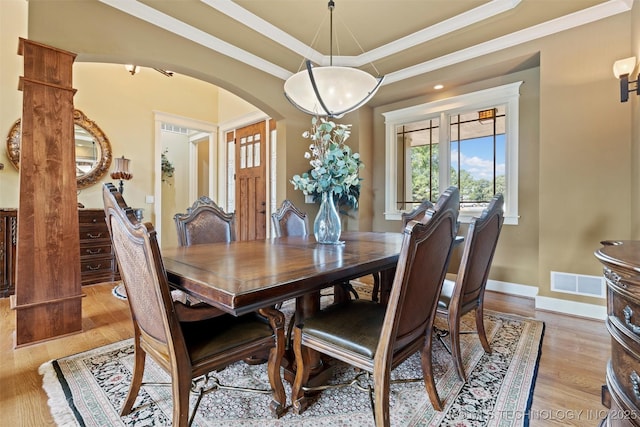 dining space with ornamental molding, light hardwood / wood-style floors, and a raised ceiling