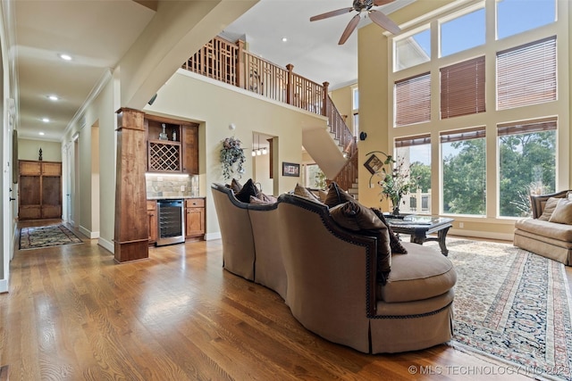 living room with a towering ceiling, wine cooler, hardwood / wood-style flooring, ornamental molding, and bar