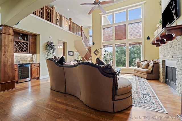 living room with wine cooler, bar, wood-type flooring, ceiling fan, and a towering ceiling