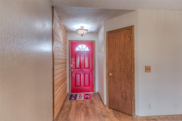 doorway to outside with wood walls, a textured ceiling, and light wood-type flooring