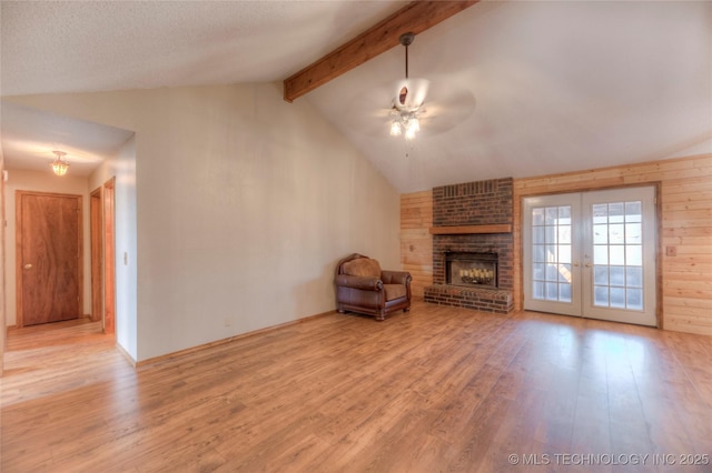 unfurnished living room with light hardwood / wood-style flooring, ceiling fan, a fireplace, lofted ceiling with beams, and french doors