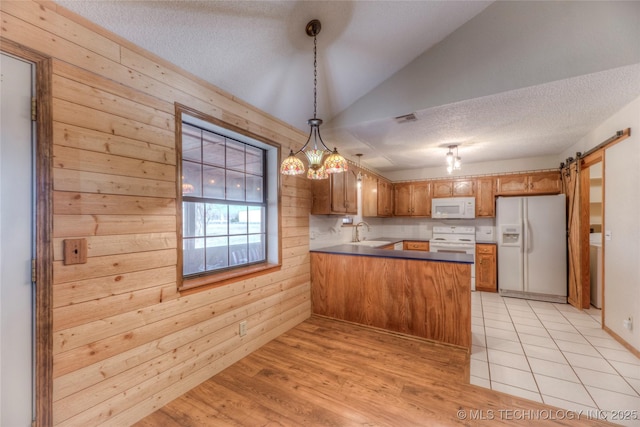 kitchen featuring white appliances, kitchen peninsula, decorative light fixtures, a barn door, and wood walls