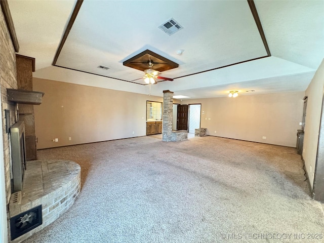 unfurnished living room with a raised ceiling, a brick fireplace, ceiling fan, and ornate columns