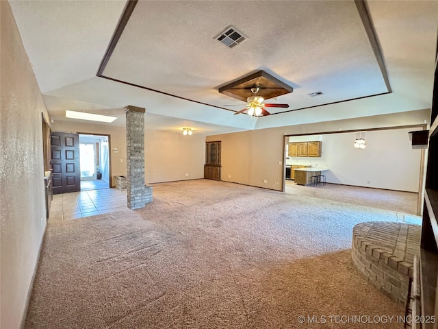 unfurnished living room featuring ceiling fan, light colored carpet, decorative columns, and a textured ceiling