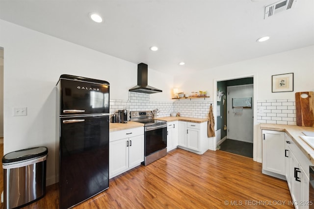 kitchen featuring stainless steel electric range, wooden counters, white cabinetry, black refrigerator, and wall chimney exhaust hood