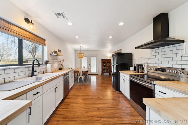 kitchen with wall chimney exhaust hood, sink, appliances with stainless steel finishes, pendant lighting, and white cabinets