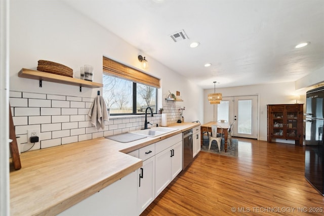 kitchen featuring decorative light fixtures, wooden counters, white cabinets, black fridge, and light wood-type flooring