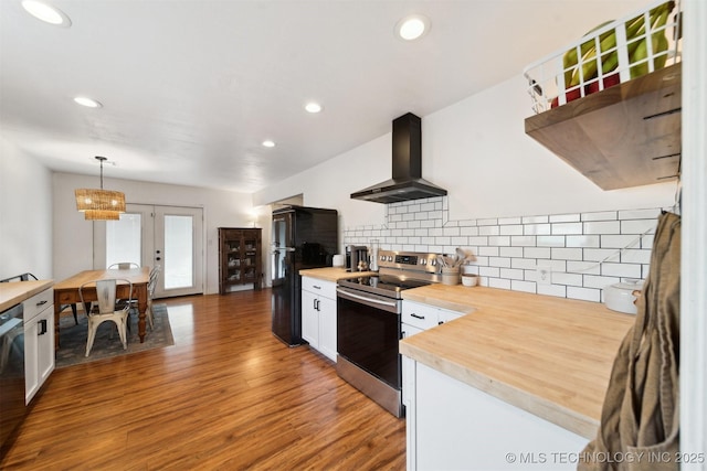 kitchen with butcher block countertops, wall chimney range hood, white cabinetry, hanging light fixtures, and black appliances