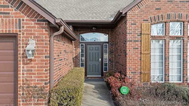 doorway to property featuring a garage, brick siding, and roof with shingles