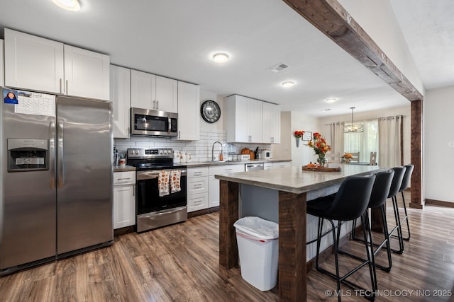 kitchen featuring stainless steel appliances, white cabinetry, a kitchen island, and hanging light fixtures