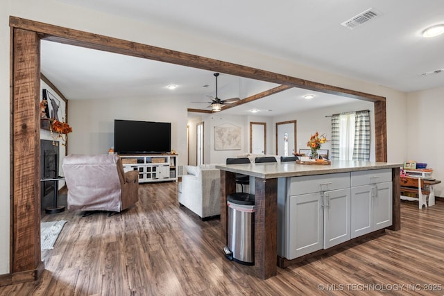 kitchen with ceiling fan, dark hardwood / wood-style floors, light stone countertops, an island with sink, and vaulted ceiling