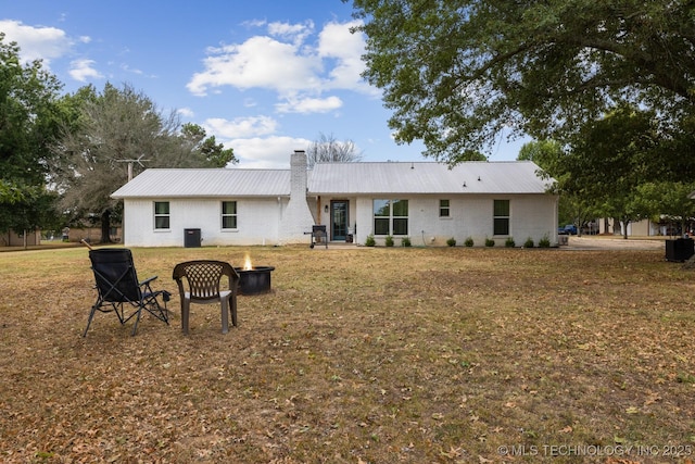 rear view of property with a yard, central AC, and a fire pit