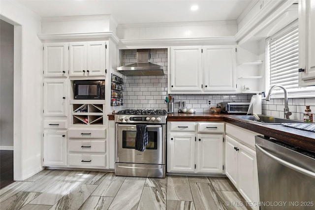 kitchen featuring appliances with stainless steel finishes, tasteful backsplash, white cabinets, wall chimney range hood, and sink