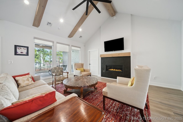 living area with wood finished floors, visible vents, a ceiling fan, a glass covered fireplace, and beamed ceiling