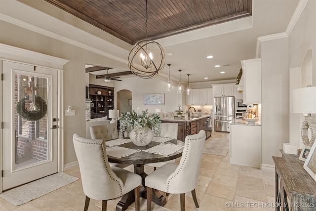 dining space featuring sink, wood ceiling, ornamental molding, ceiling fan with notable chandelier, and a raised ceiling