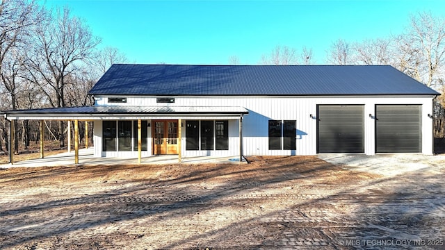 back of house featuring dirt driveway, a porch, a standing seam roof, metal roof, and a garage